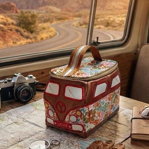 May include: A colorful, retro-style cooler bag shaped like a vintage van, with a floral pattern and the word "LOVE". The scene includes a map, compass, camera, gloves, and sunglasses, suggesting a road trip.
