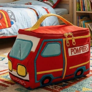 Peut inclure: Sac à déjeuner isotherme rouge et blanc en forme de camion de pompiers, avec des détails jaunes et bleus. Le sac a une poignée jaune et le mot "Pompiers" sur le côté. Le sac est posé sur un tapis coloré.