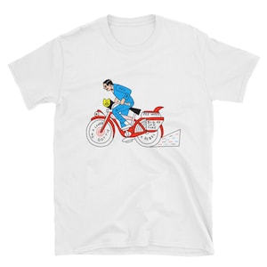May include: A white t-shirt featuring a red, blue and yellow illustration of a person riding a bicycle. The bicycle has the words "I'm a loner Dottie" on the front wheel and "Pee Wee's Big Adventure A Rebel" on the back wheel.