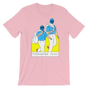 May include: Pink t-shirt with a graphic of two figures wearing blue and white wrestling masks. The figures are holding towels that say "I'll be back" and "I'll be back" and are labeled "Danny" and "Arnold". The graphic is set in a yellow rectangle with the text "TERMINATOR® TWINS" below.