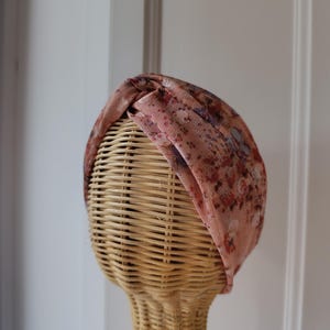 Puede incluir: Una diadema turbante de color rosa con un diseño anudado y un estampado floral.