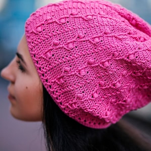 A crochet pink hat is showcased on the side profile of a woman's head.