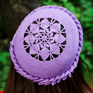 A purple crocheted hat with a delicate floral design on a top side of the beanie. The hat is made with a soft, lightweight yarn and has a comfortable fit.