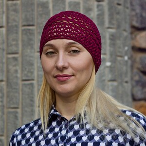 May include: A woman with blonde hair is wearing a burgundy crocheted beanie and a black and white heart patterned shirt.