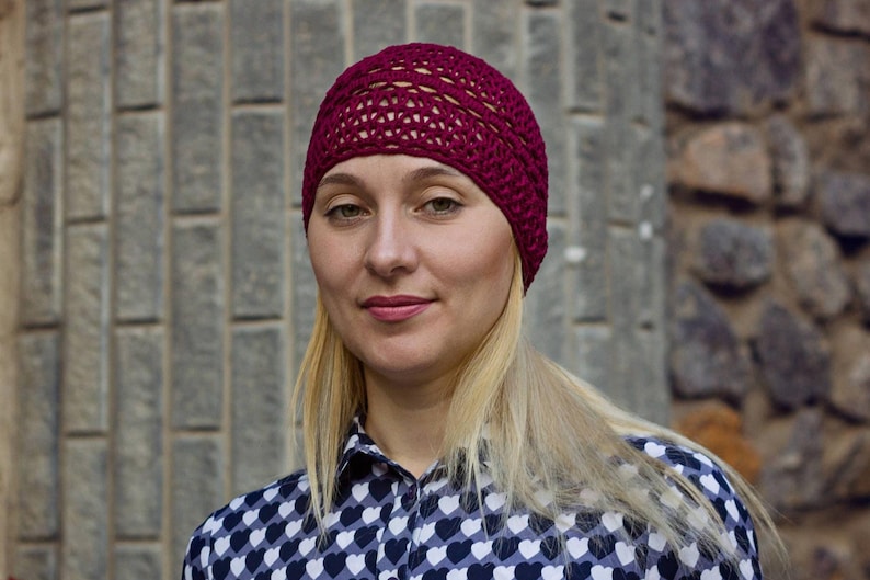 May include: A woman with blonde hair is wearing a burgundy crocheted beanie and a black and white heart patterned shirt.