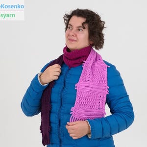 May include: A handmade, crocheted scarf in shades of purple and pink. The scarf features a fringed edge and a textured design. The image also includes the text "@itwasyarn" and "KateKosenko".