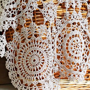 Beige lace crochet scarf gracefully draped and hanging from a light straw picnic basket, showcasing its lightweight and elegant design.