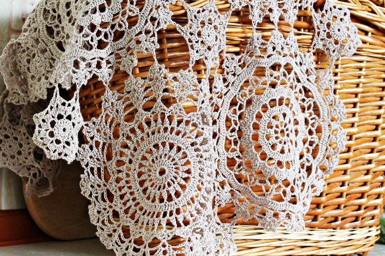 Beige lace crochet scarf gracefully draped and hanging from a light straw picnic basket, showcasing its lightweight and elegant design.