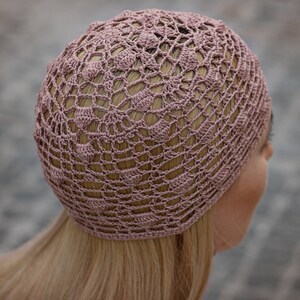 May include: A close-up of a crocheted hat in a dusty rose colour. The hat is made with a delicate openwork pattern.