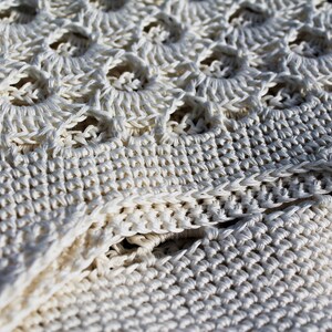 May include: Close-up of a white crocheted fabric with a textured pattern. The fabric is made of thick yarn and has a delicate, lacy look.