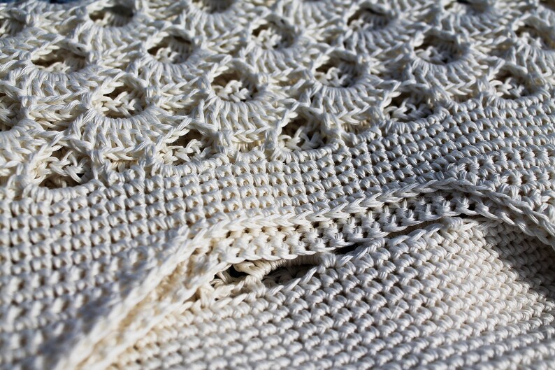 May include: Close-up of a white crocheted fabric with a textured pattern. The fabric is made of thick yarn and has a delicate, lacy look.