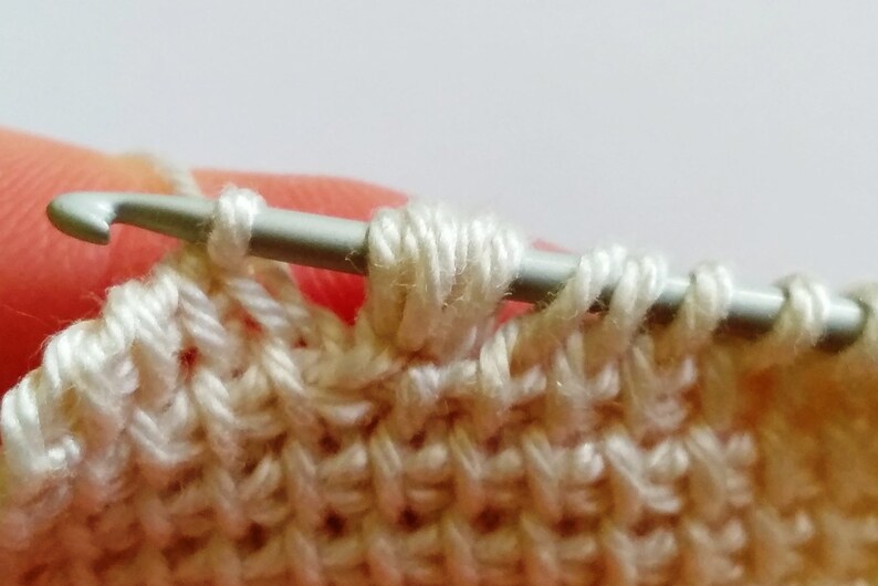 The process of crocheting Tunisian stitch using fine weight light-colored yarn.