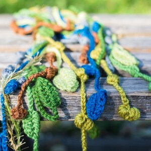 May include: A crocheted scarf with green, blue, brown, and yellow leaves. The scarf is made of yarn and is a handmade craft.