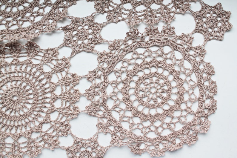 Beige crochet scarf with intricate as-you-go round motifs, photographed hanging in full view on a white background.