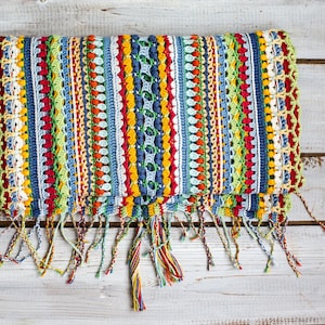 Handmade crochet blossom scarf with tassels in primary colors on wooden background