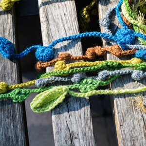 May include: A close-up of a wooden surface with colorful crocheted yarn strands. The yarn is in shades of green, blue, yellow, and brown. The yarn is arranged in a random pattern, creating a textured and visually appealing design.