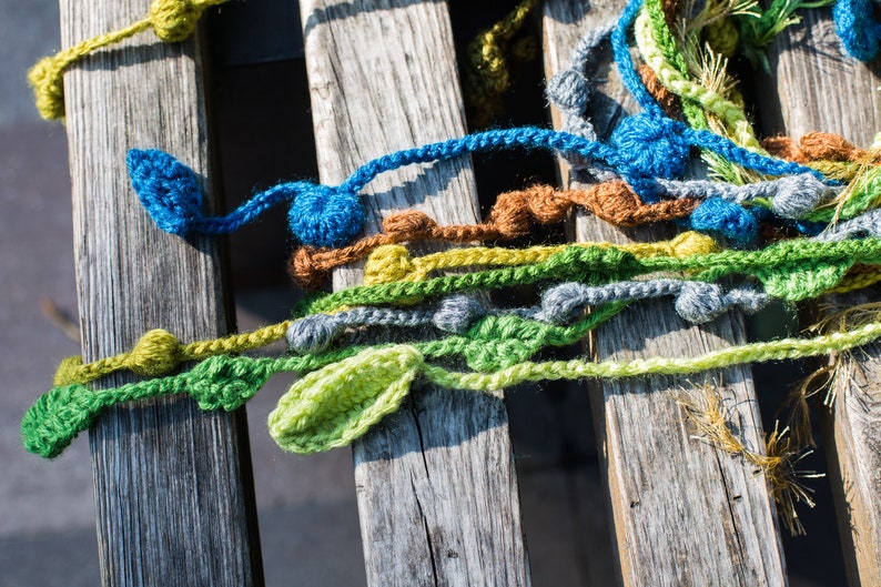May include: A close-up of a wooden surface with colorful crocheted yarn strands. The yarn is in shades of green, blue, yellow, and brown. The yarn is arranged in a random pattern, creating a textured and visually appealing design.