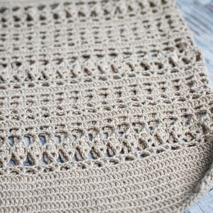 May include: Close-up of a beige crocheted fabric with a delicate pattern. The fabric is made of a natural fiber and has a soft, textured surface.
