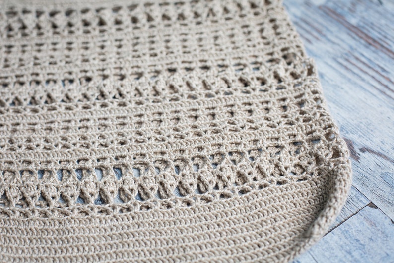 May include: Close-up of a beige crocheted fabric with a delicate pattern. The fabric is made of a natural fiber and has a soft, textured surface.