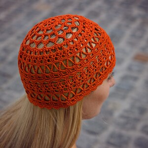 The woman is showcasing an orange crocheted lace hat in profile.