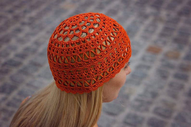 The woman is showcasing an orange crocheted lace hat in profile.