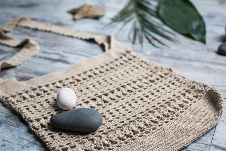 May include: A beige crocheted tote bag with two smooth stones inside. One stone is white and the other is gray.