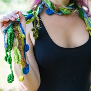 May include: A crocheted necklace with green, blue, and brown yarn. The necklace has a long, flowing design with multiple strands and beads.