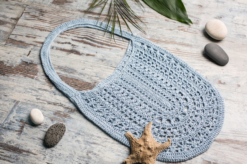 Soft blue handmade bag with one strap, flat lay with stones and starfish – feminine and minimal beach accessory