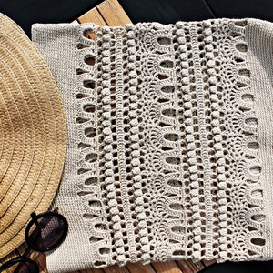 May include: A beige crocheted tote bag with a woven pattern. The bag is lying on a wooden surface next to a straw hat and apples.