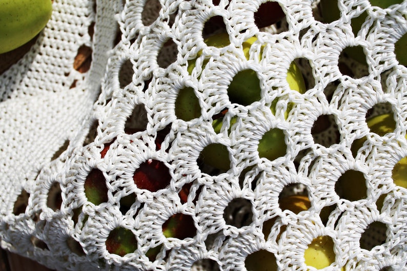 May include: White crocheted bag with a variety of apples inside. The apples are red, green, and yellow.