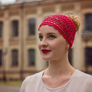 May include: A woman with a red crocheted headband and a white shirt. She is looking to the side and smiling.