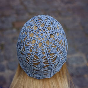 A cotton crochet light blue hat on the head, viewed from the back of the head. Geometric lacy pattern.