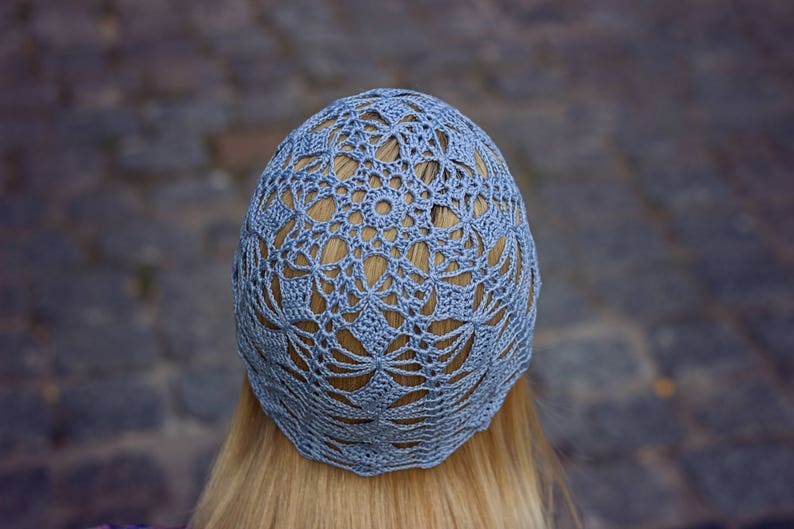 A cotton crochet light blue hat on the head, viewed from the back of the head. Geometric lacy pattern.