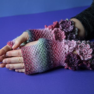 May include: A pair of fingerless gloves with a pink, purple, and green striped pattern. The gloves have crocheted flowers on the cuffs.