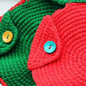 May include: Two crocheted bags with a round shape and a flap closure. One bag is green with a wooden button and the other is red with a blue button.
