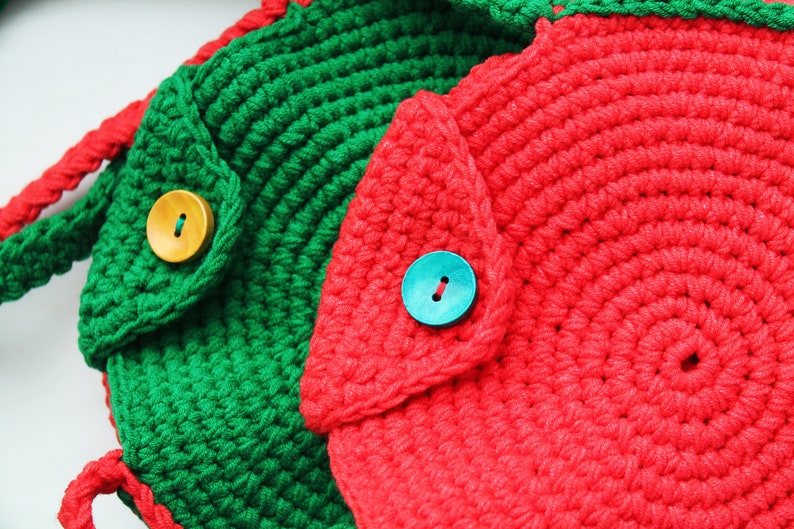 May include: Two crocheted bags with a round shape and a flap closure. One bag is green with a wooden button and the other is red with a blue button.