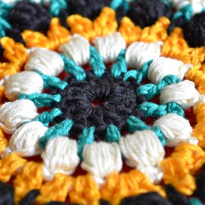May include: Close-up of a crocheted mandala with a central black circle surrounded by turquoise, white, and yellow yarn.