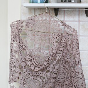 Elegant beige crochet scarf wrapped as it would be worn on shoulders, hanging on a hanger with soft light background.