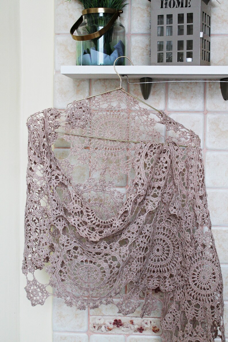 Elegant beige crochet scarf wrapped as it would be worn on shoulders, hanging on a hanger with soft light background.