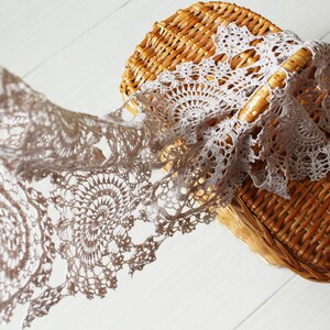Soft beige crochet scarf cascading from a woven straw picnic basket, emphasizing its delicate motifs and summer-ready style.