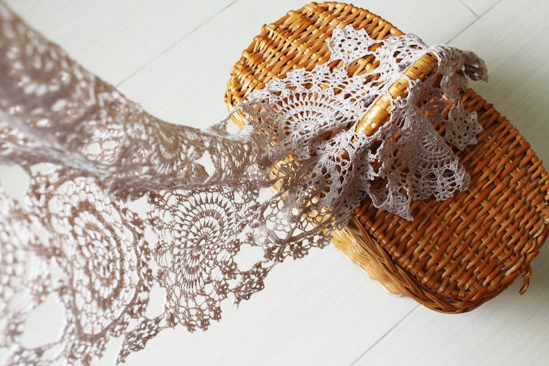 Soft beige crochet scarf cascading from a woven straw picnic basket, emphasizing its delicate motifs and summer-ready style.