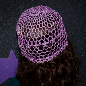 May include: A purple crochet hat with a delicate openwork design. The hat is made of soft yarn and has a comfortable fit.