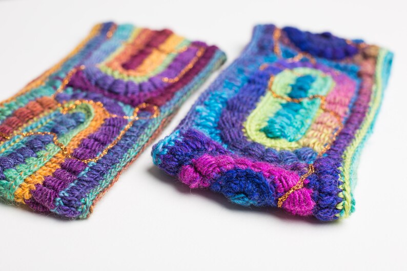May include: Two colorful crocheted headbands with a rainbow pattern and gold accents. The headbands are made with a variety of different colored yarns.
