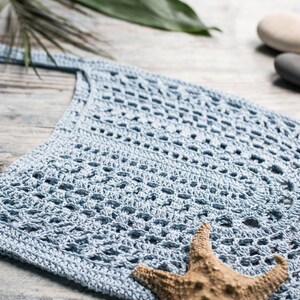 Lacy summer crochet bag in pastel blue, displayed flat with beachy decor – crochet design by Ukrainian designer Veselunka