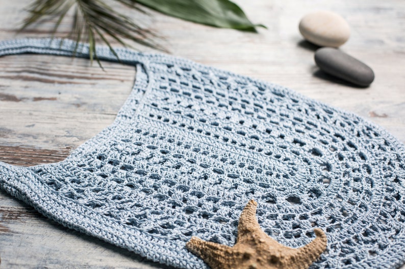 Lacy summer crochet bag in pastel blue, displayed flat with beachy decor – crochet design by Ukrainian designer Veselunka