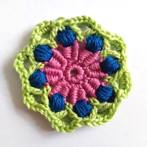 May include: A crocheted flower with a pink center and green and blue outer layers.