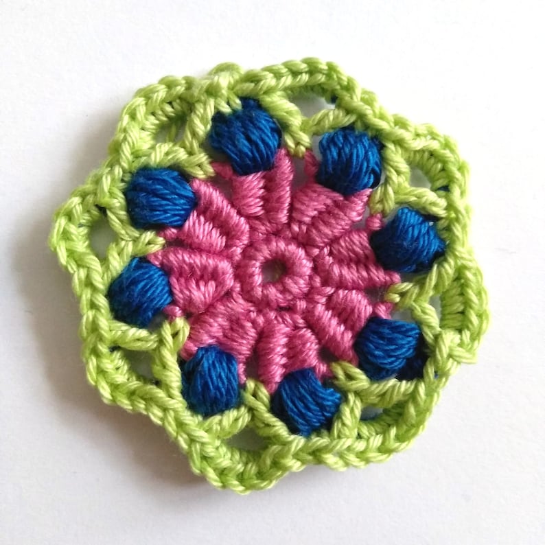 May include: A crocheted flower with a pink center and green and blue outer layers.