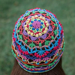 May include: A colorful crocheted hat with a multi-colored mandala design. The hat is made with a variety of bright colors, including red, orange, yellow, green, blue, and purple.