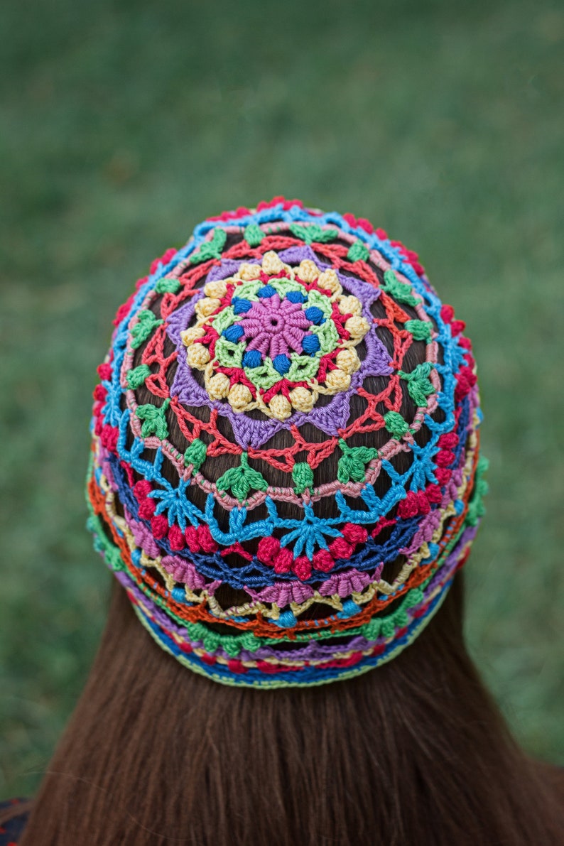 May include: A colorful crocheted hat with a multi-colored mandala design. The hat is made with a variety of bright colors, including red, orange, yellow, green, blue, and purple.