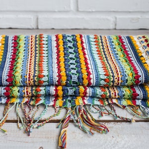 A scarf made by hand using crochet techniques, featuring tassels in vibrant primary colors.